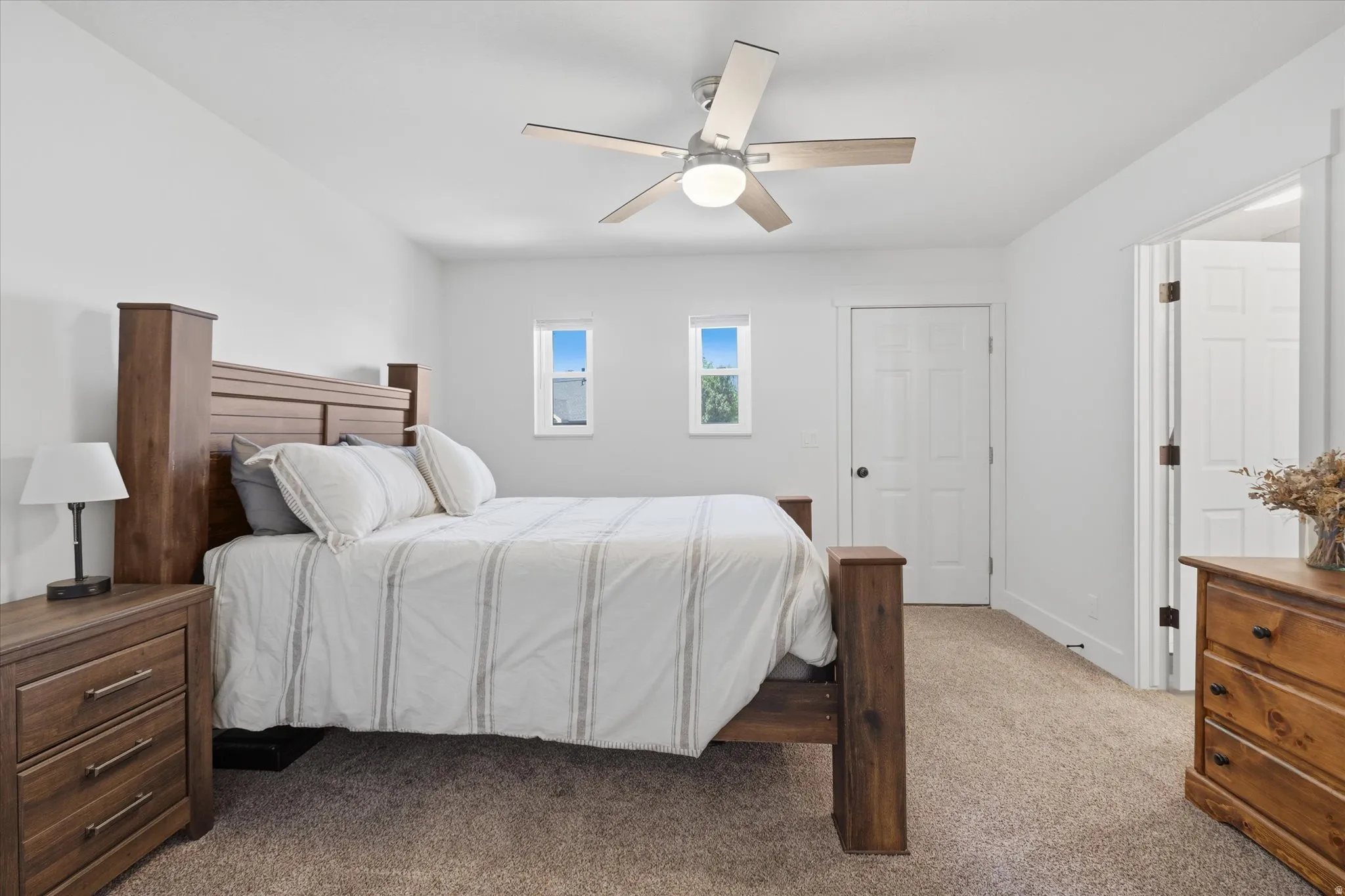 Neutral-toned bedroom featuring twin windows, plush carpet flooring, a ceiling fan with integrated lighting, and white trim throughout