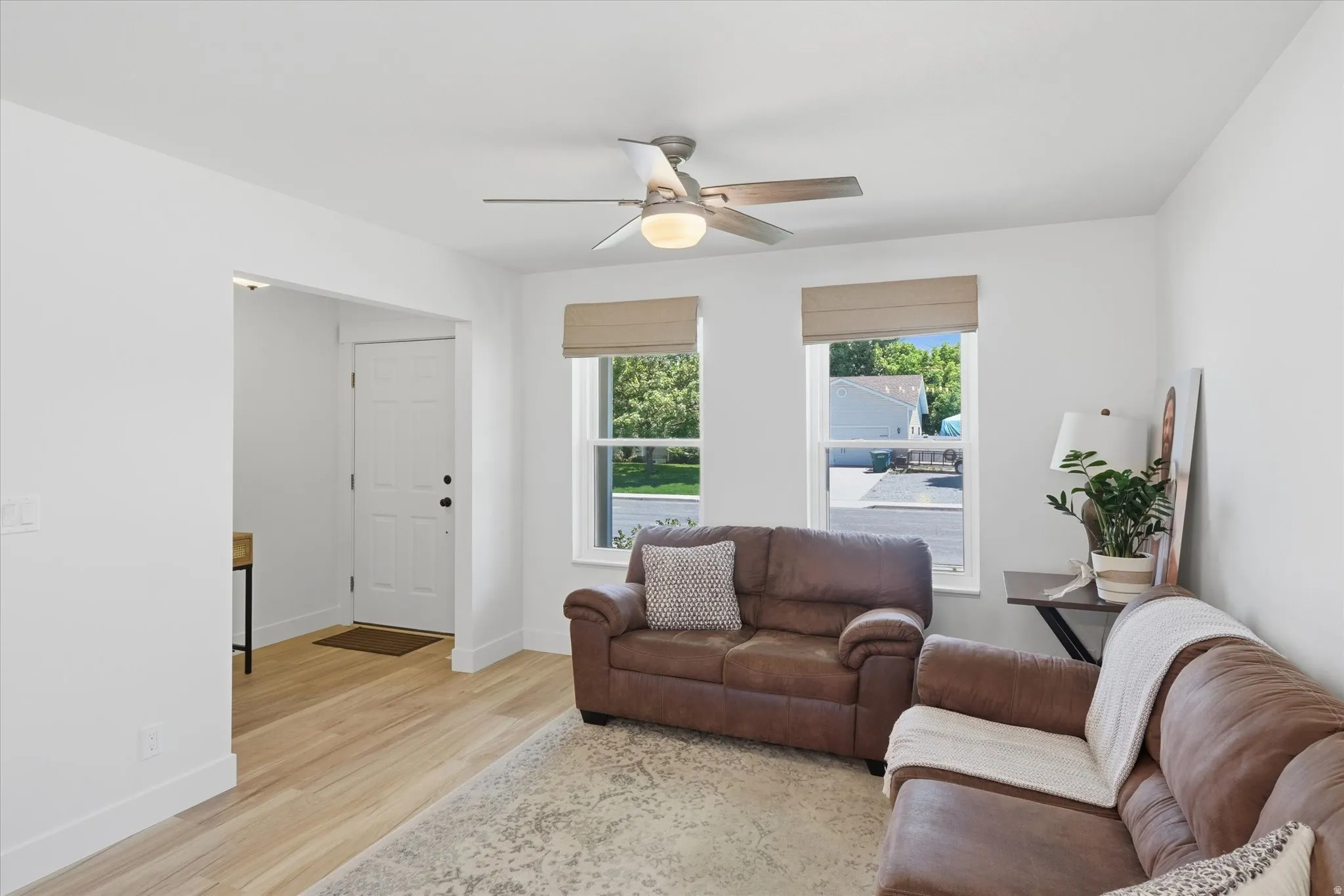 Bright living space featuring light wood-finish flooring, white baseboards, and a modern ceiling fan