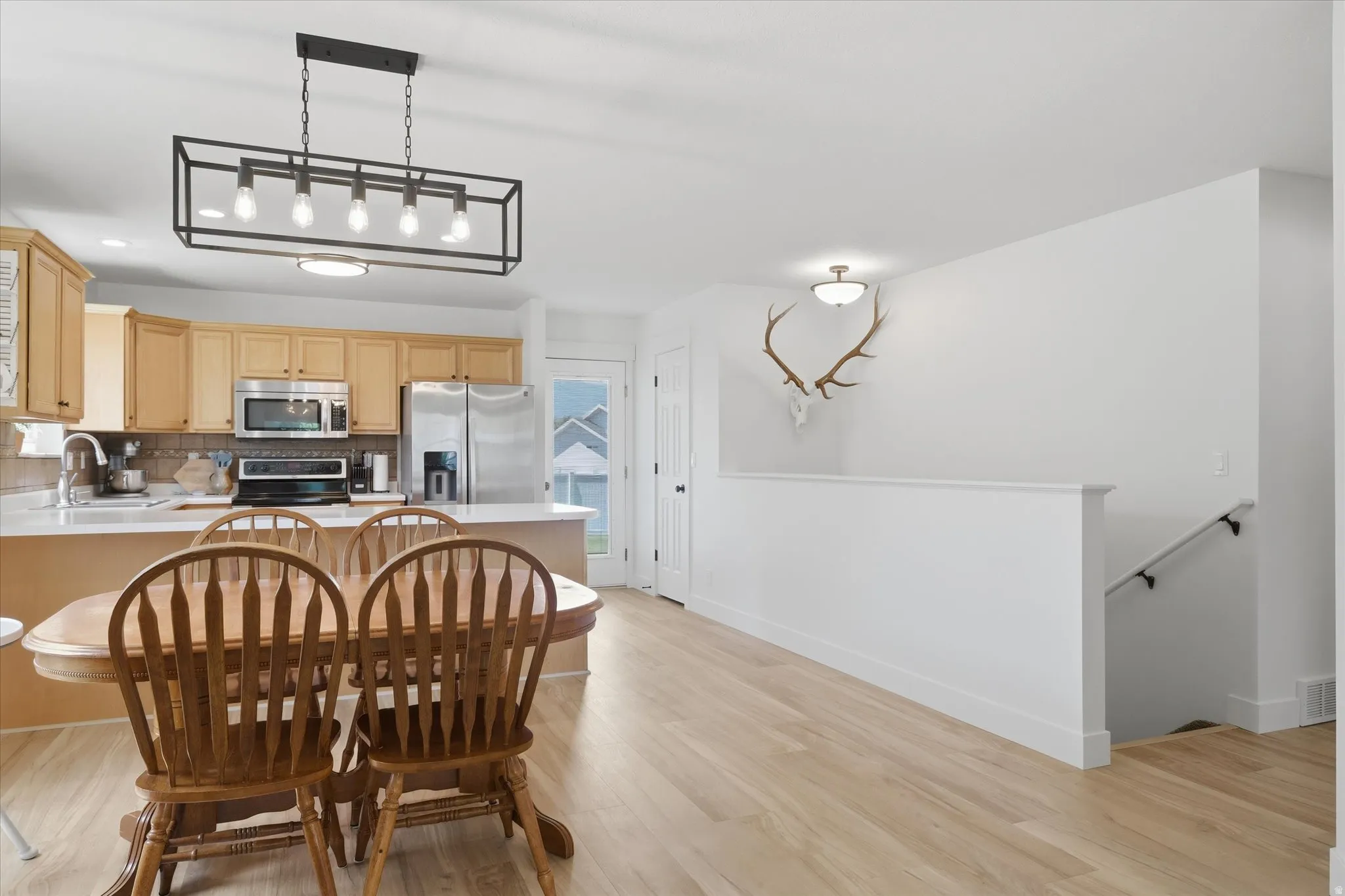 Open-concept kitchen and dining area featuring light wood-finish flooring, a kitchen island with white countertop, recessed lighting, and stainless steel appliances