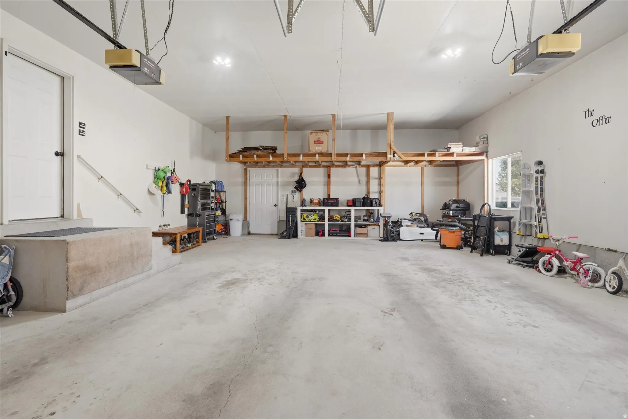 Spacious garage featuring a concrete floor, overhead shelving, and multiple light fixtures