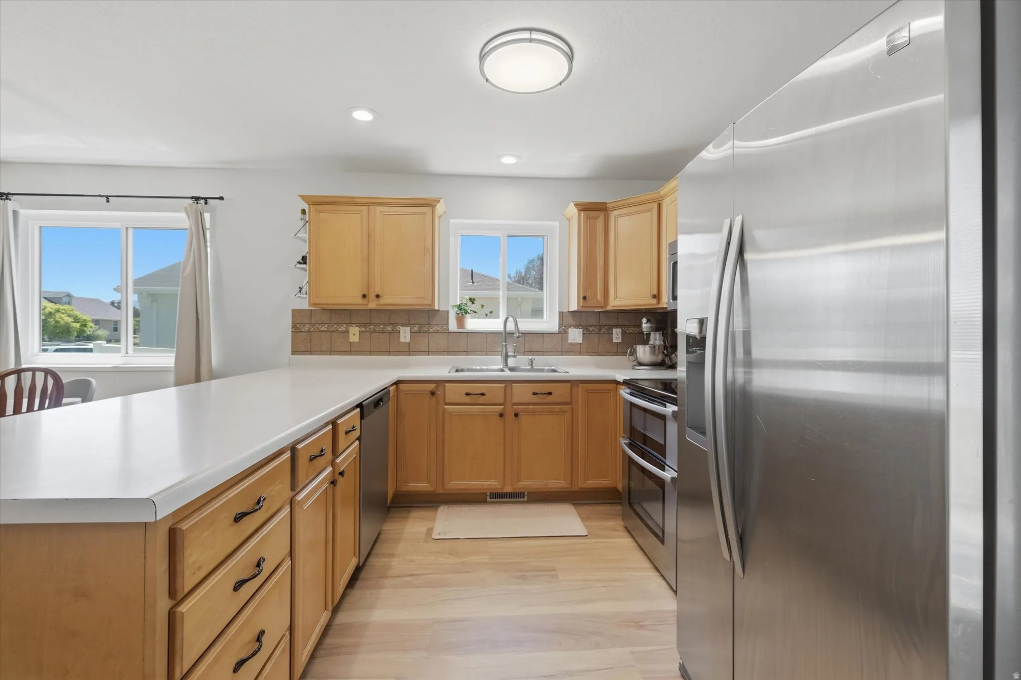 Kitchen featuring light wood-finish flooring, light wood cabinetry, white countertops, and a tiled backsplash