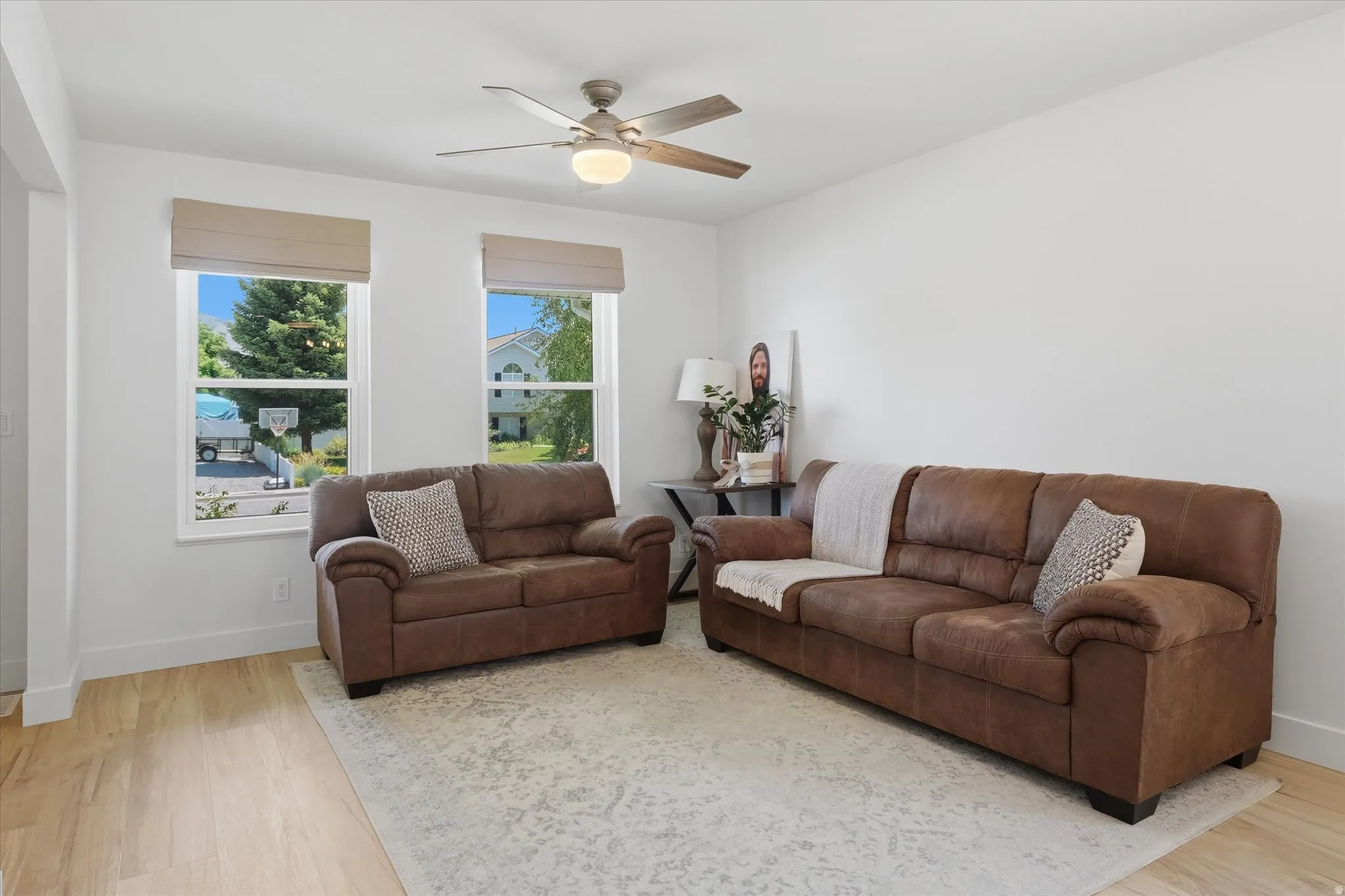 Bright living area featuring wood-finish flooring, white walls, and a ceiling fan with integrated lighting