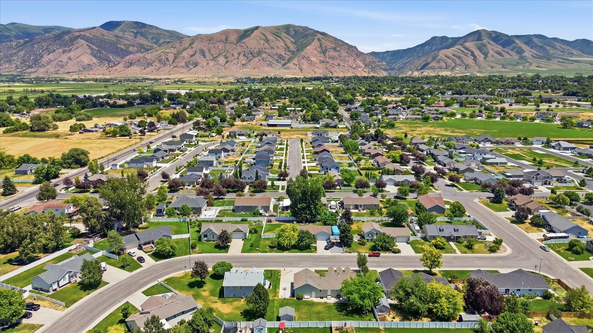 Residential neighborhood featuring a grid-pattern street layout, established homes with varied rooflines, extensive green landscaping, and distant mountain ranges