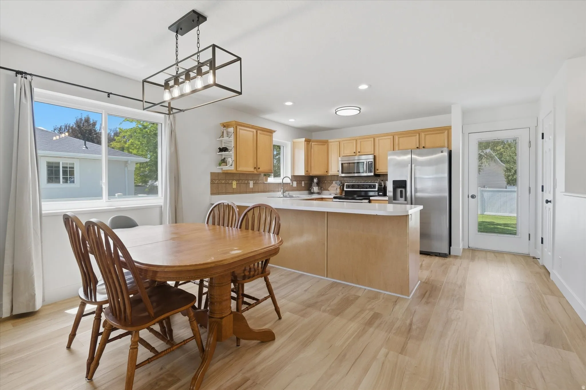Open-concept kitchen and dining area featuring light wood-finish flooring, a kitchen island with a white countertop, and light natural wood cabinetry