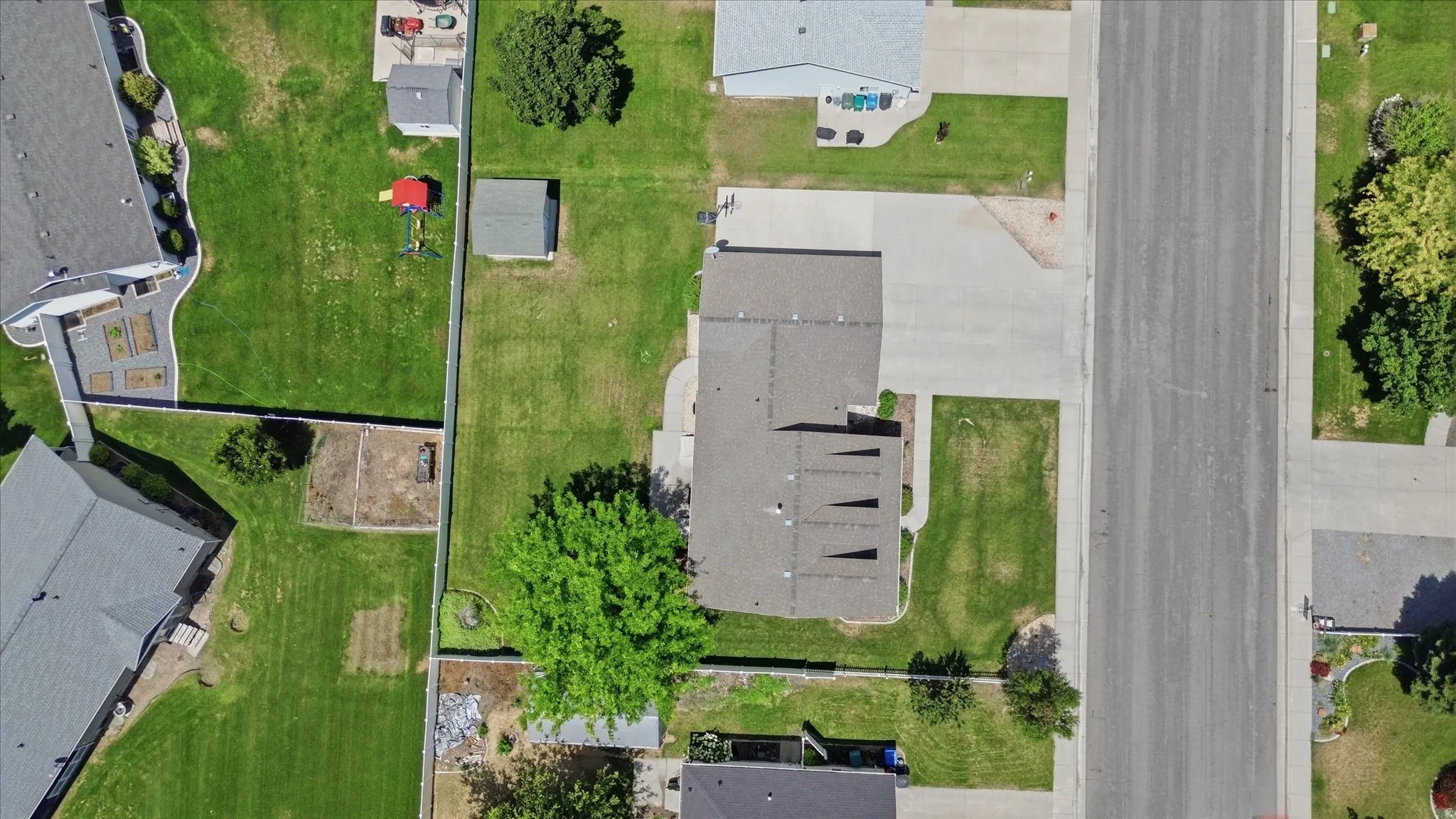 Overhead perspective showcasing a residential property with a gray shingle roof, expansive green lawn, mature trees, and a paved driveway