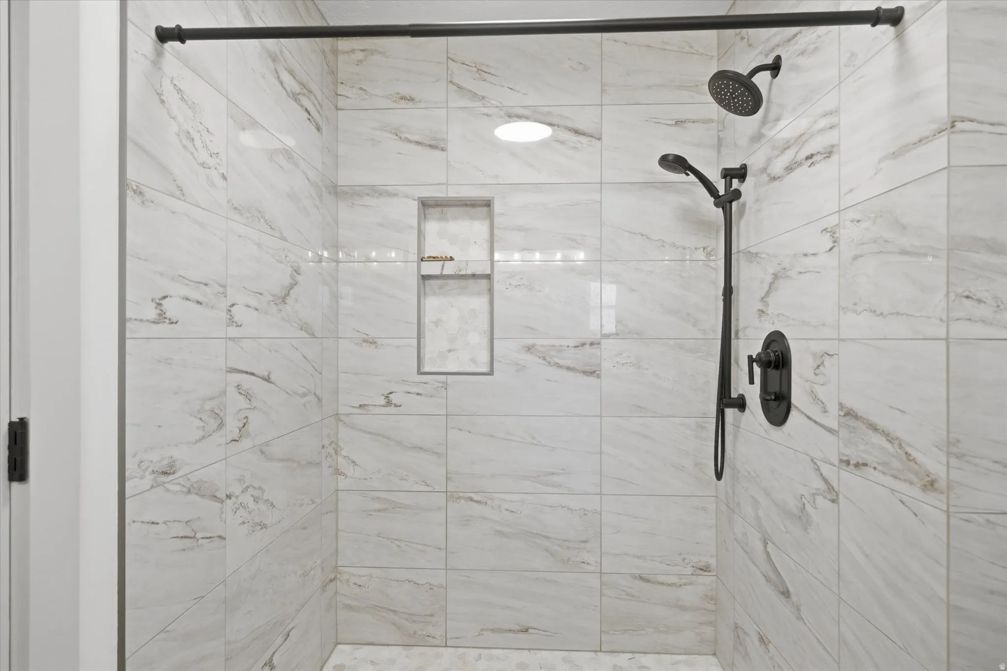Walk-in shower featuring large format white and gray variegated tile, matte black shower fixtures, a built-in shower niche, and recessed ceiling lighting