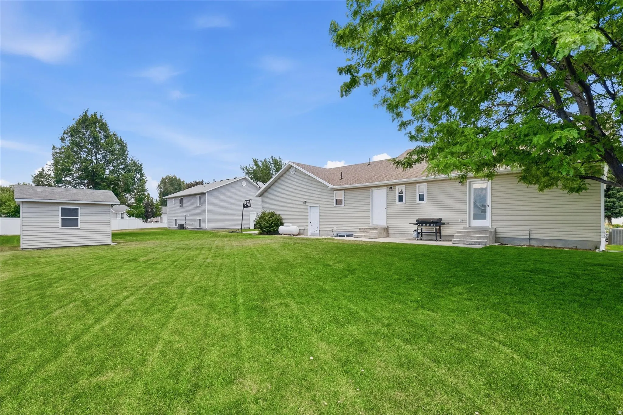 Expansive rear yard featuring a large green lawn, a detached storage shed, and a concrete patio