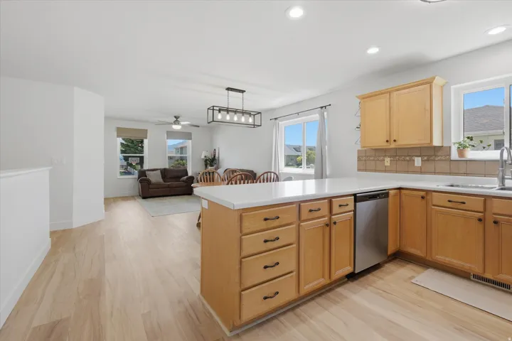 Kitchen with light wood cabinetry, white countertops, stainless steel dishwasher, and square tile backsplash
