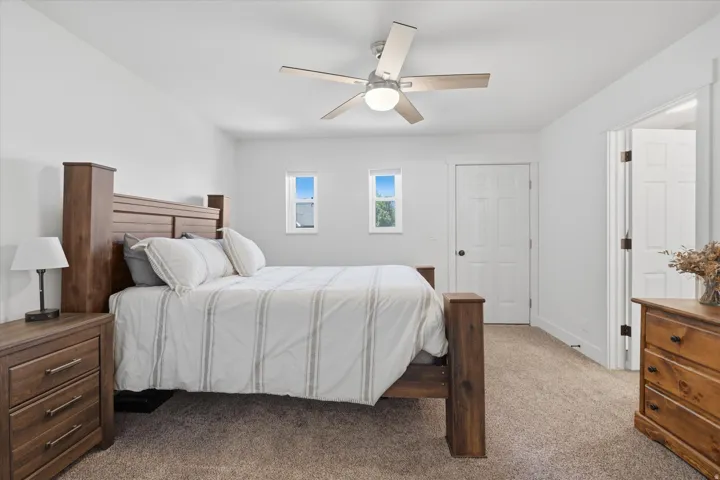 Neutral-toned bedroom featuring twin windows, plush carpet flooring, a ceiling fan with integrated lighting, and white trim throughout