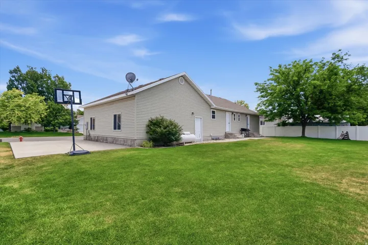 Expansive rear yard featuring a large concrete patio, a substantial lawn area, and mature perimeter trees