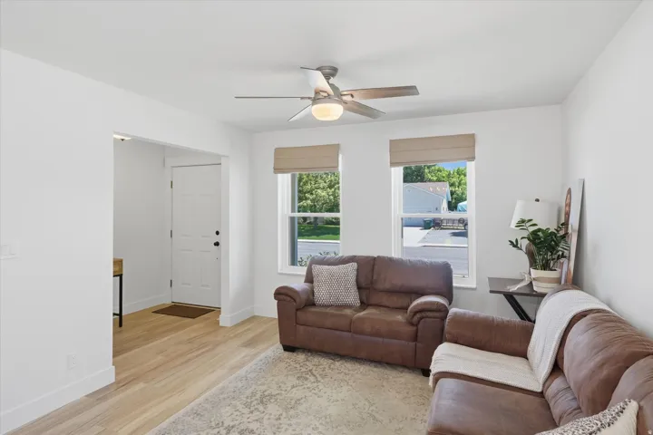Bright living space featuring light wood-finish flooring, white baseboards, and a modern ceiling fan