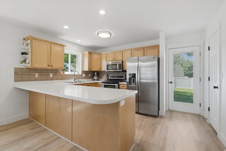 Kitchen featuring wood-finish flooring, light wood cabinetry, stainless steel appliances, and a white countertop