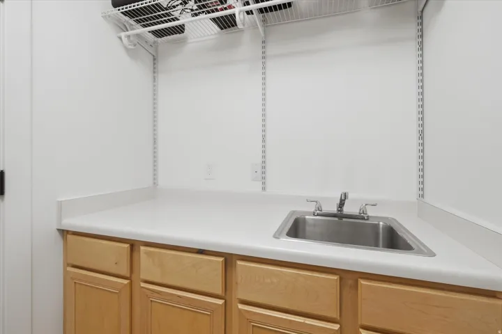 Utility room featuring a stainless steel sink, light wood-finish cabinetry, and a white countertop