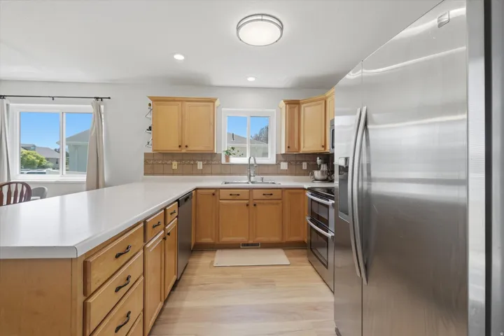 Kitchen featuring light wood-finish flooring, light wood cabinetry, white countertops, and a tiled backsplash