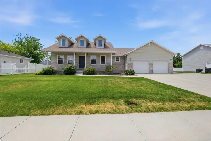 Single-story residence featuring a covered front porch, three dormer windows, a two-car garage, brick veneer accents, and a front lawn