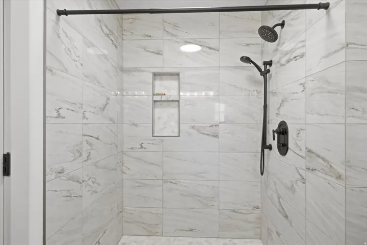 Walk-in shower featuring large format white and gray variegated tile, matte black shower fixtures, a built-in shower niche, and recessed ceiling lighting