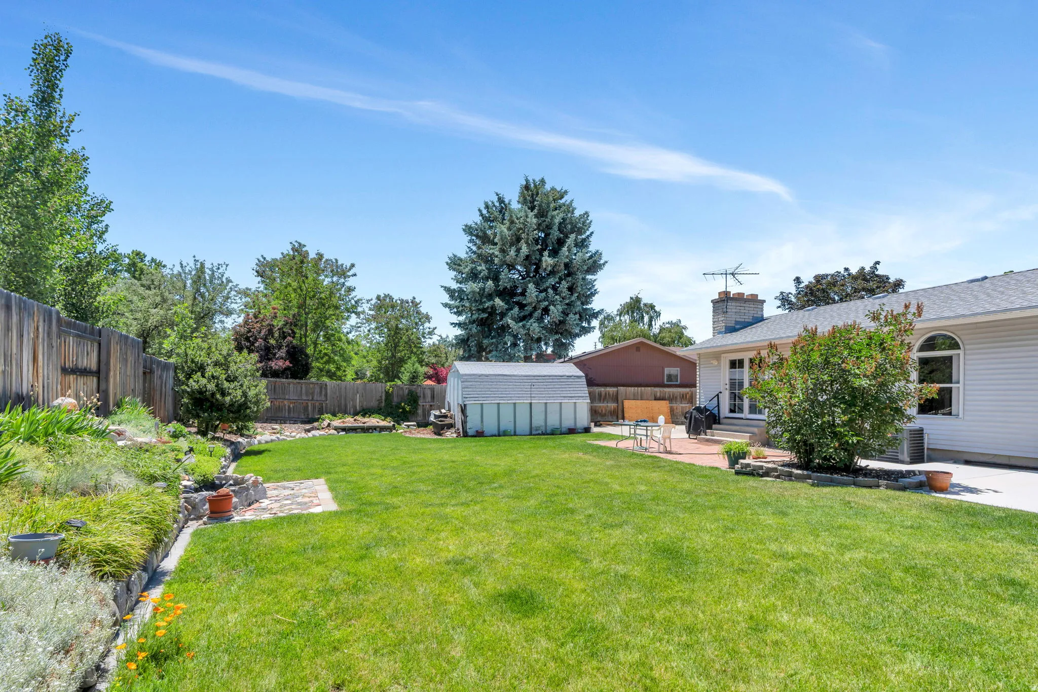 Expansive lawn area featuring a paved patio, a storage shed, and a privacy fence