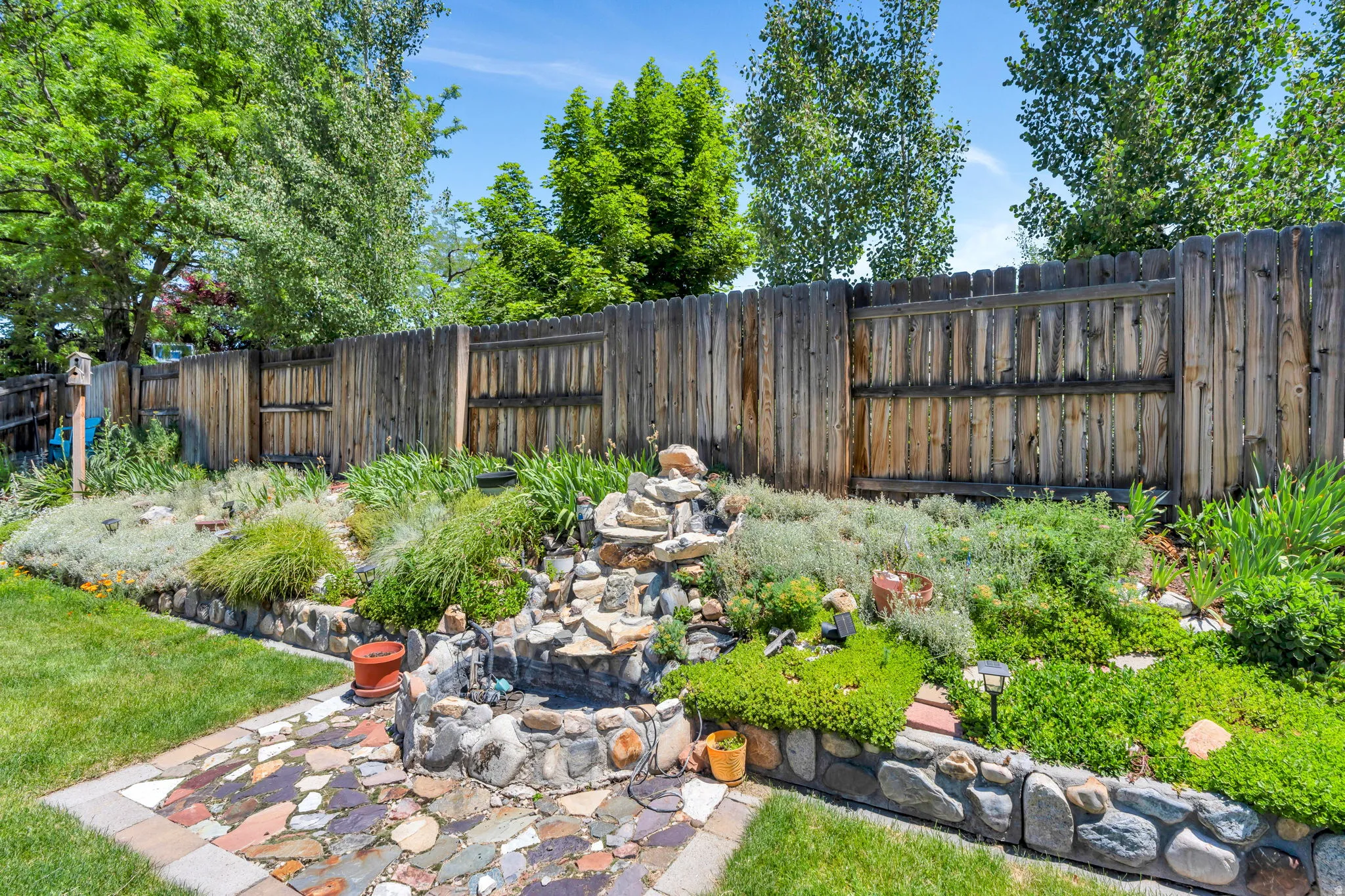 Tiered landscaping featuring a stone water feature, a flagstone patio, and a wood privacy fence