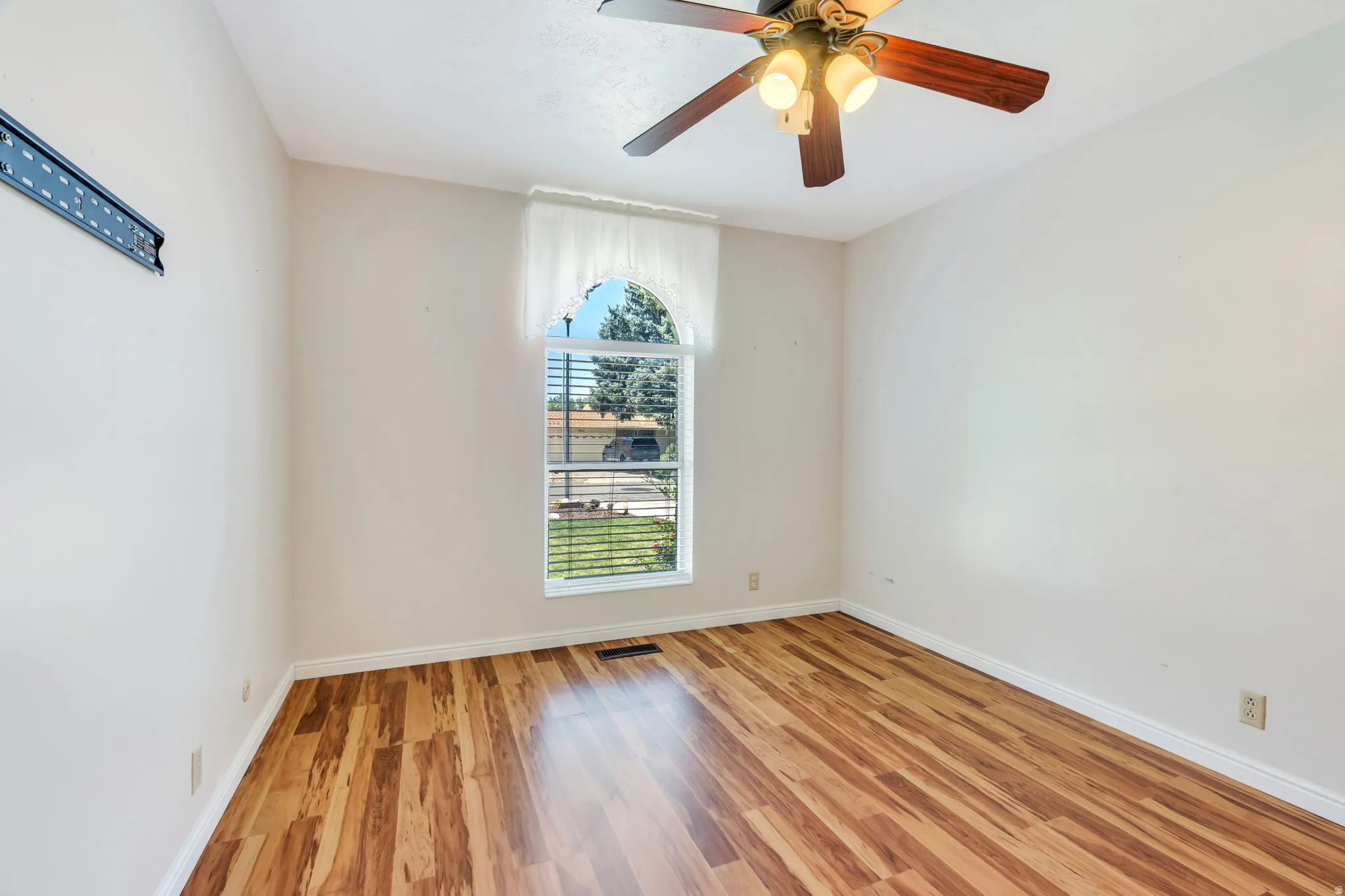 Room featuring wood-finish flooring, a ceiling fan with light fixture, and an arched window with blinds