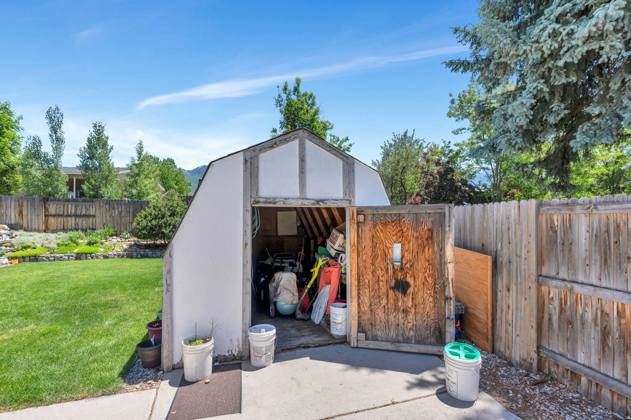 Gable-roof storage shed featuring a wood-panel door, concrete pad, and surrounding gravel landscaping