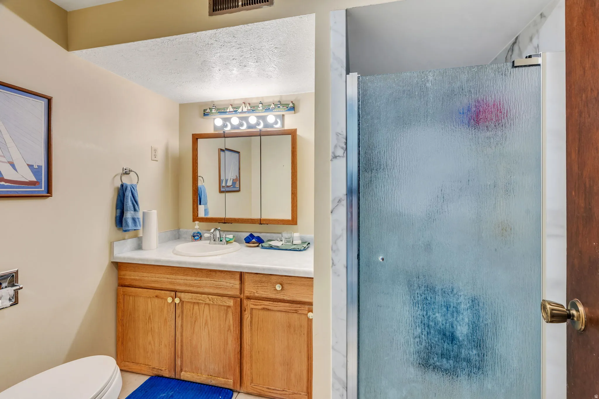 Bathroom featuring a light-toned vanity with wood-finish cabinetry, a single basin sink, and a mirrored medicine cabinet