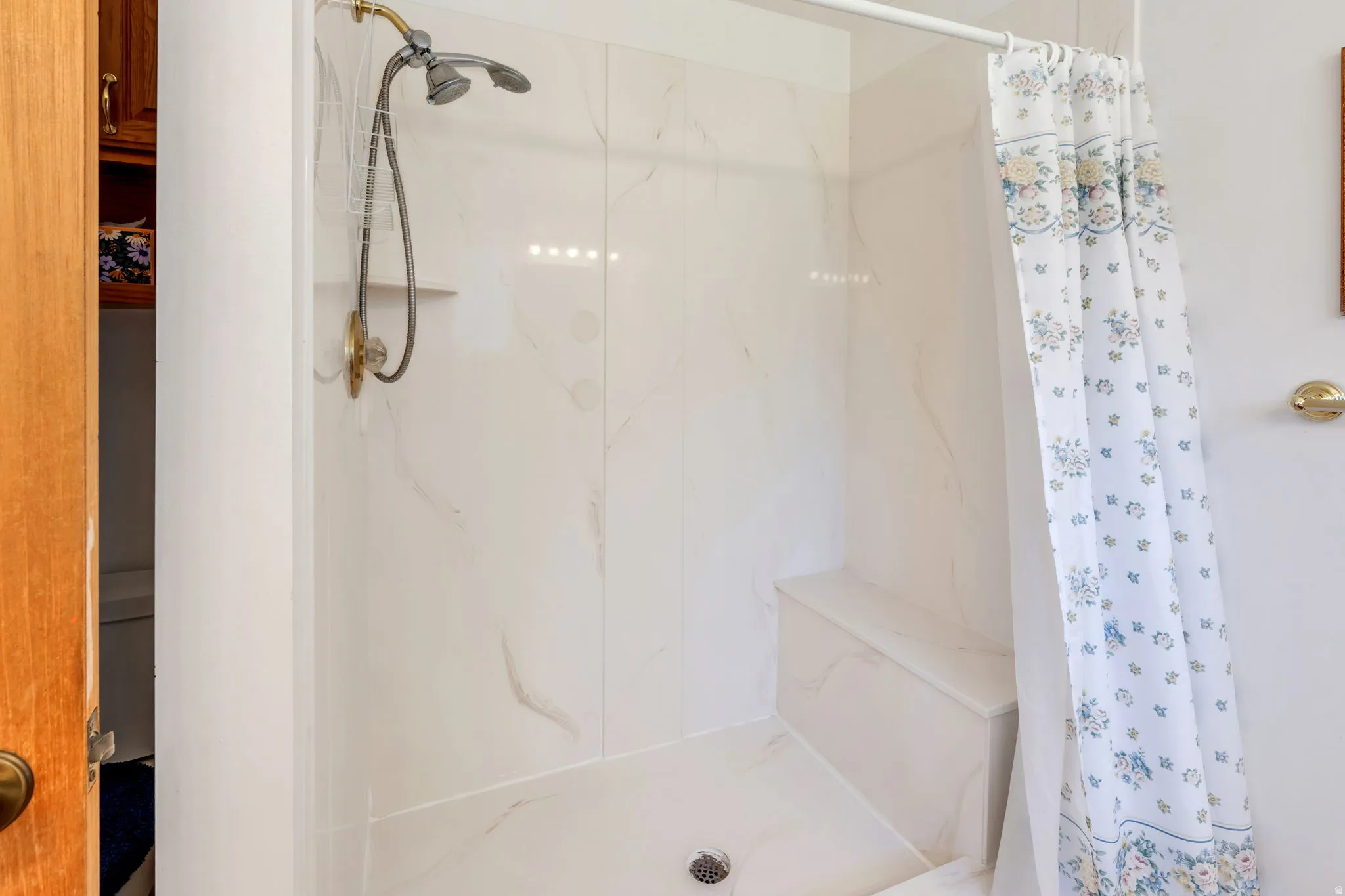 Shower enclosure featuring white paneling with subtle veining, a built-in bench, and a dual-head shower fixture