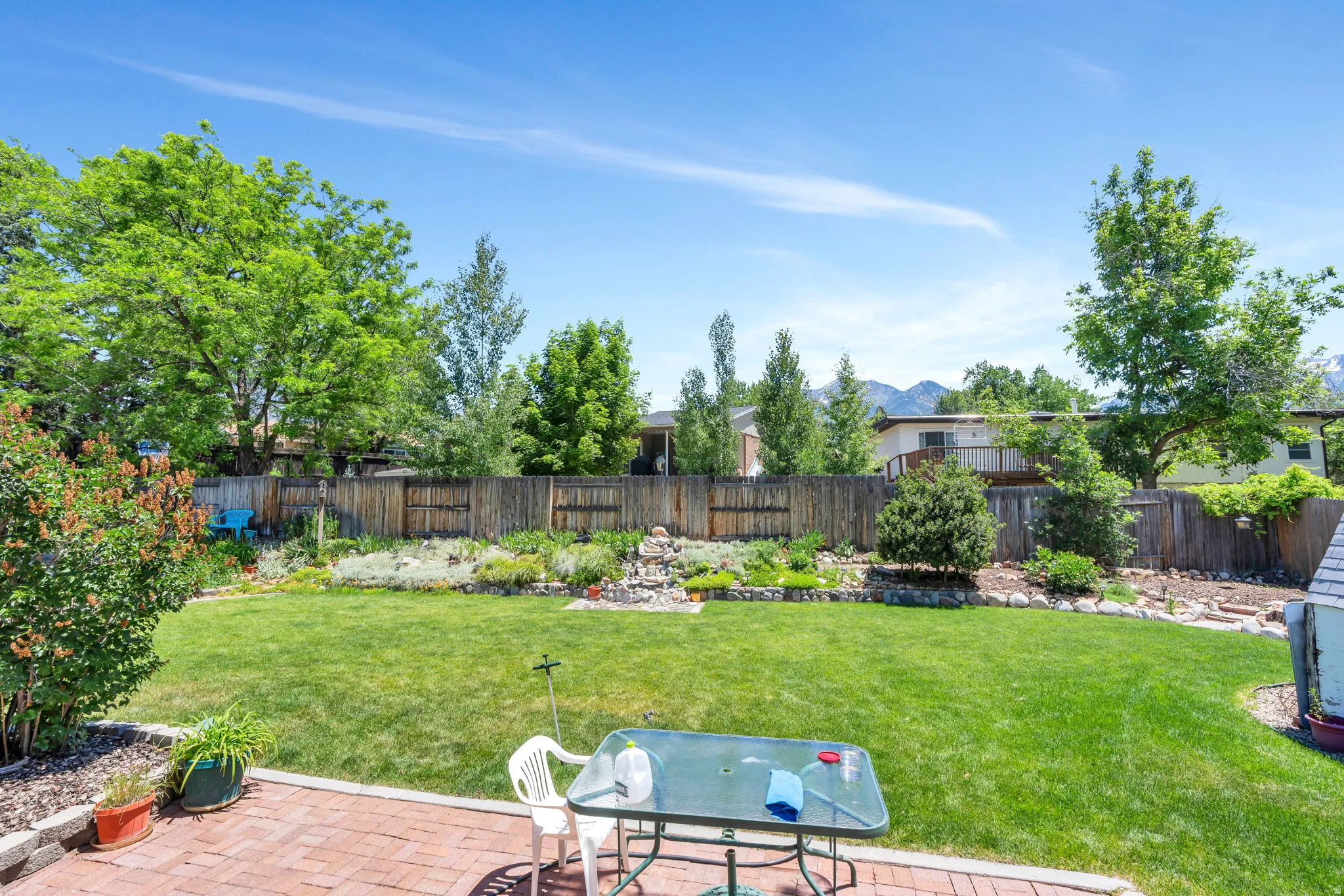 Expansive backyard featuring a large brick paver patio, a manicured lawn, and mature perimeter trees