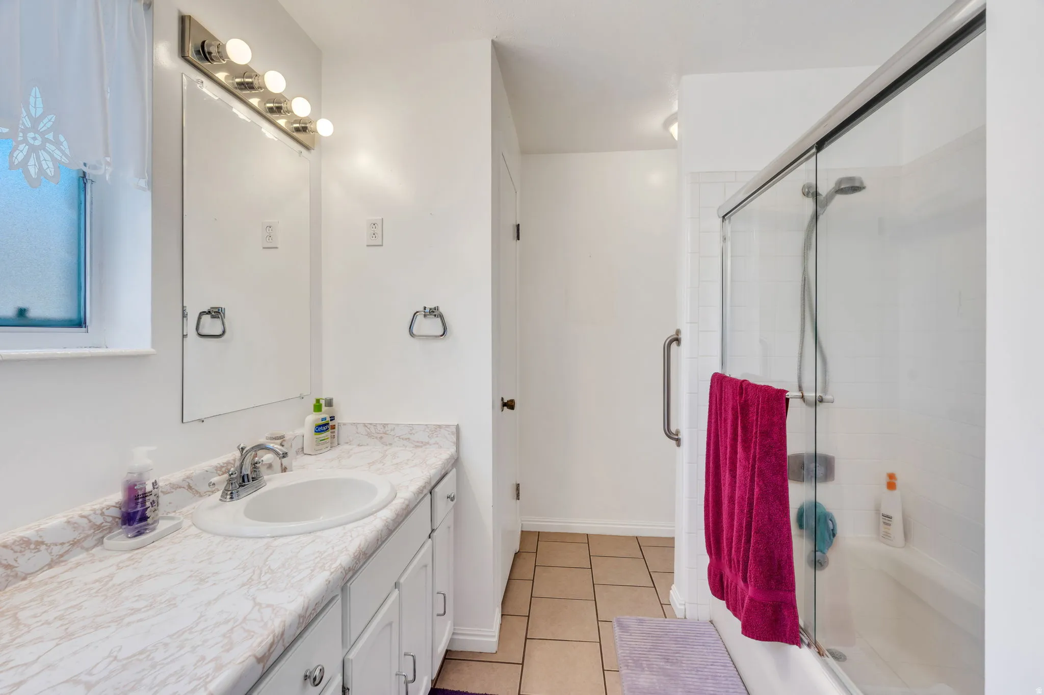 Bathroom featuring a single vanity with a white countertop and undermount sink, a large mirror, a chrome light fixture with five bulbs, and a combination shower/tub with a glass sliding door
