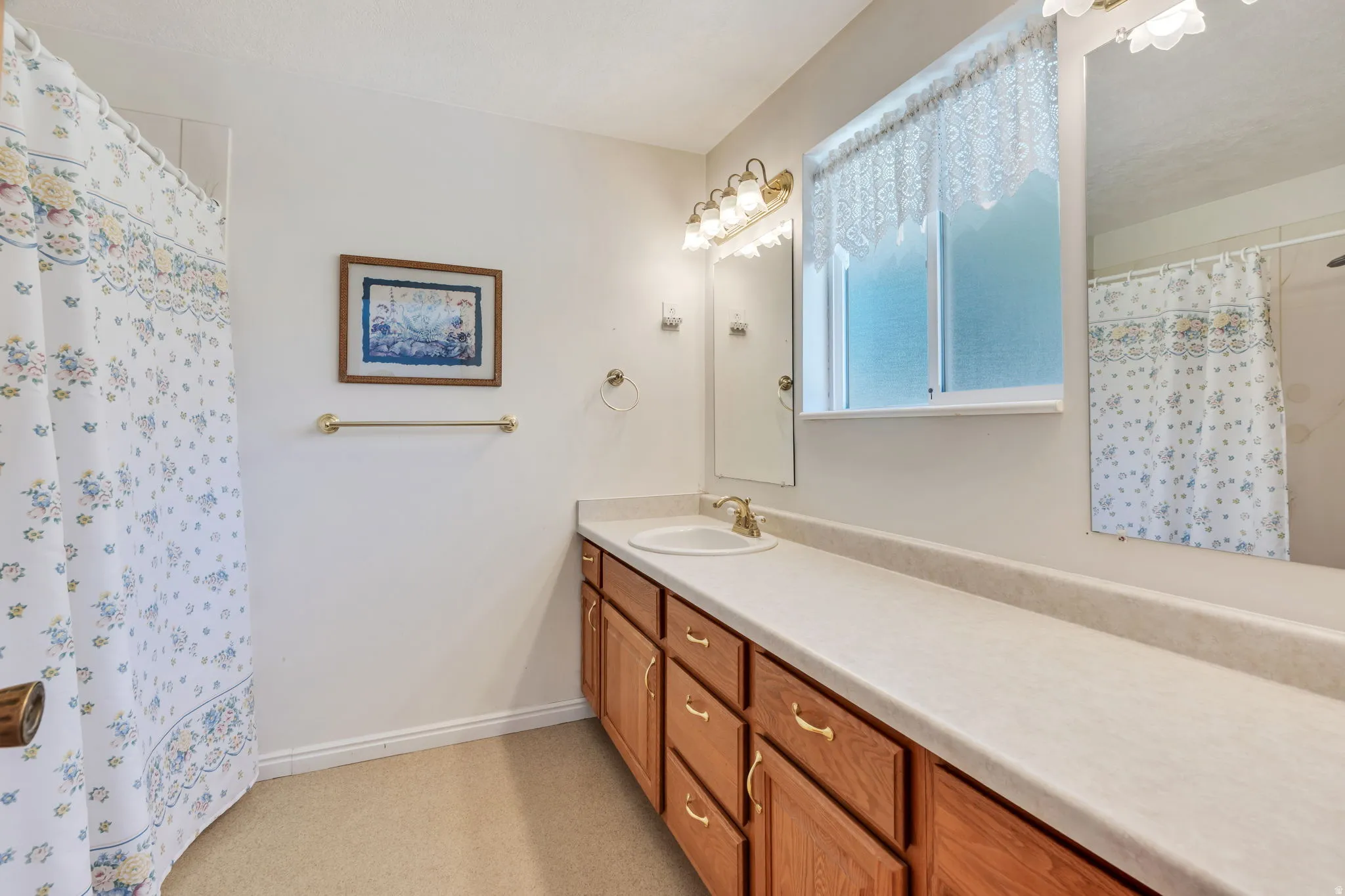 Bathroom featuring a light-toned countertop, wood-finish cabinetry with brass hardware, and a single basin sink