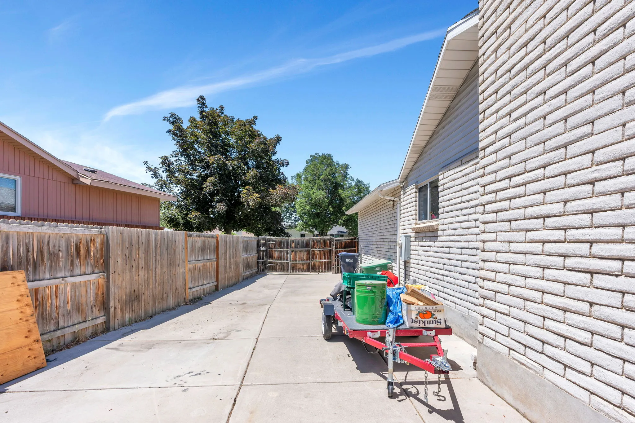 Concrete driveway extending alongside the property, featuring a wood fence boundary and mature trees in the background