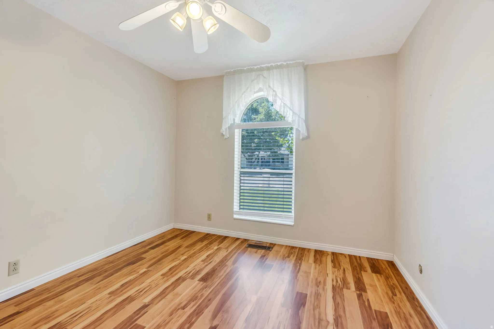 Room featuring wood-finish flooring, a white ceiling fan with integrated lighting, and an arched window with horizontal blinds