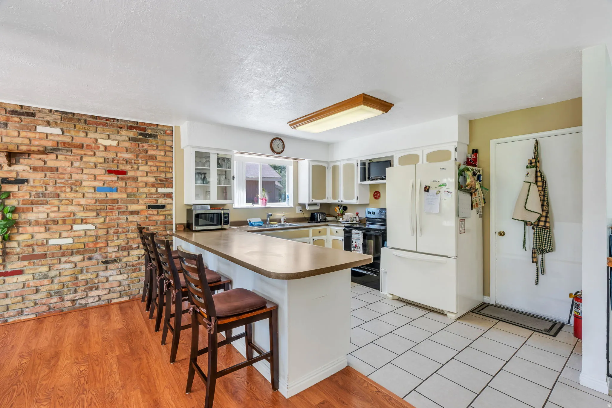 Open-concept kitchen featuring white cabinetry, a breakfast bar with seating, a white tiled floor, and a brick accent wall with wood-finish flooring