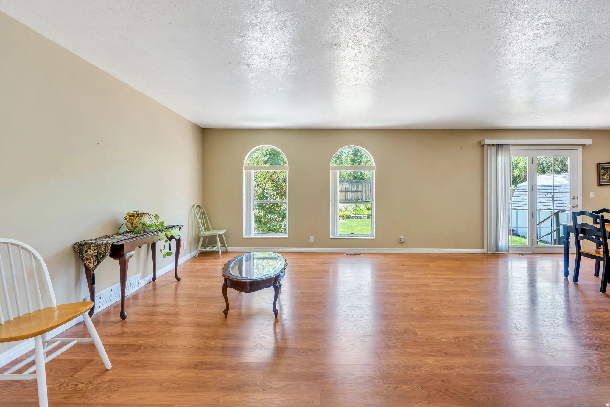 Spacious open-concept room featuring wood-finish flooring, neutral wall tones, and two arched windows