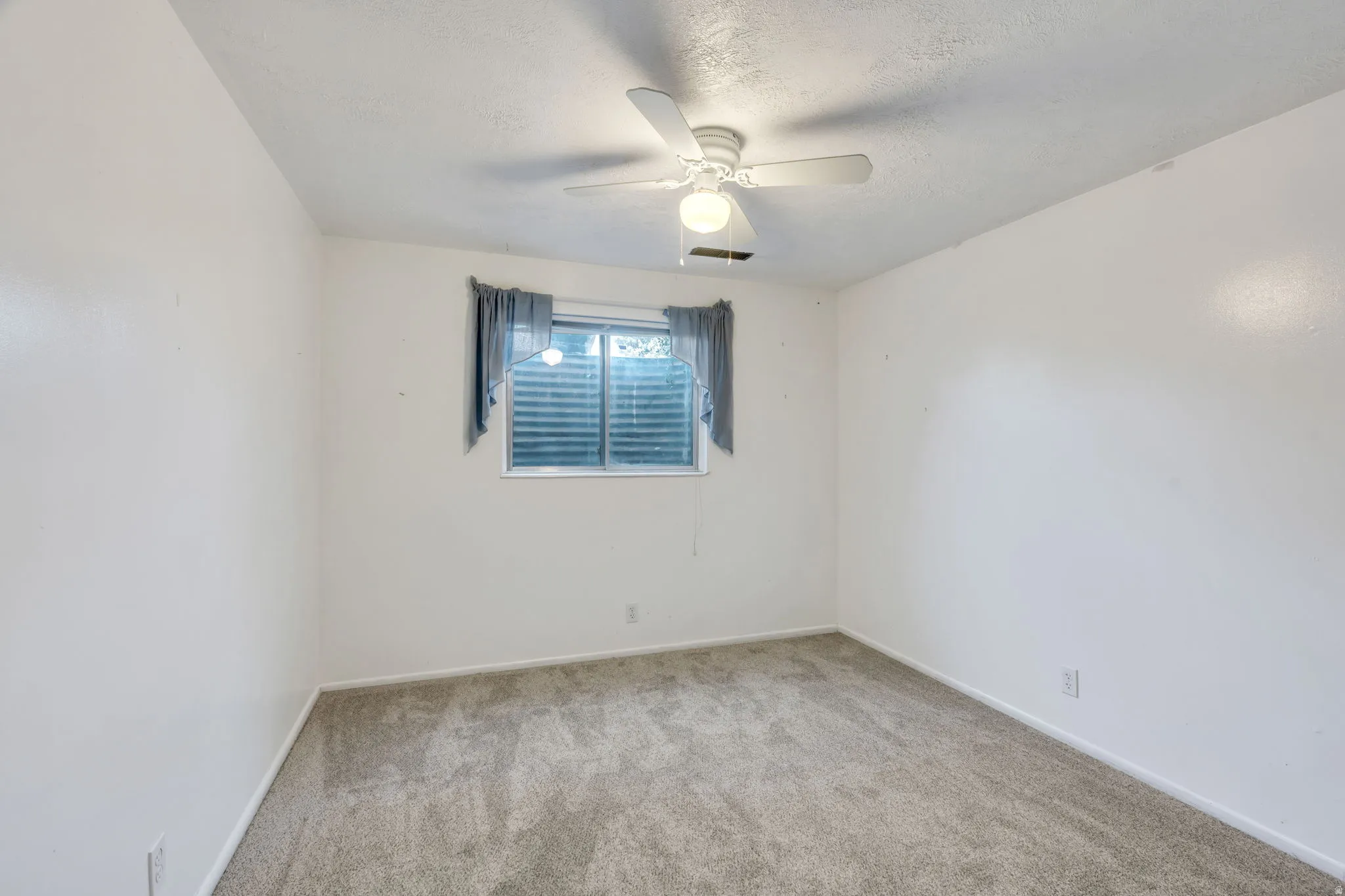 Spacious room featuring neutral carpet flooring, a window with horizontal blinds, and a ceiling fan with integrated lighting