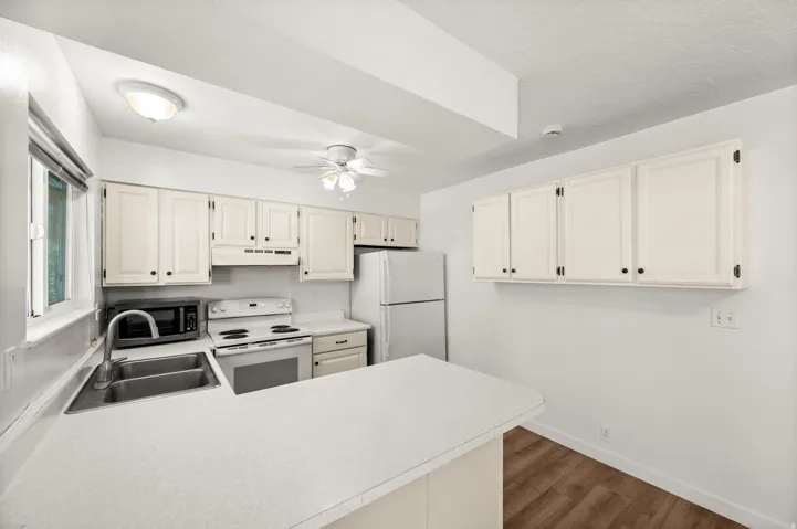 Kitchen featuring light-toned cabinetry, a double basin stainless steel sink, white electric range, and a ceiling fan with integrated lighting