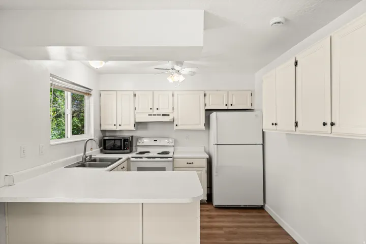 Kitchen featuring white cabinetry, light countertops, wood-finish flooring, a double basin sink, and a window