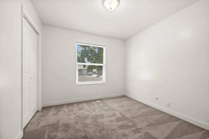 Neutral wall paint, textured carpet flooring, bi-fold closet doors, ceiling-mounted light fixture, and a window with blinds