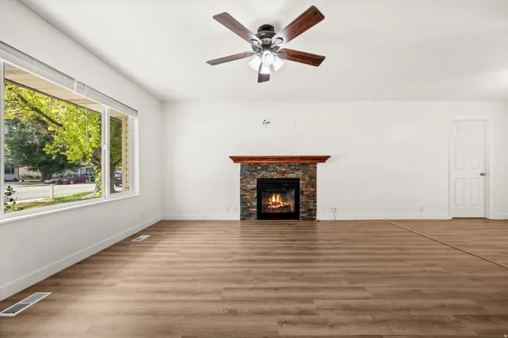 Spacious room featuring wood-finish flooring, a stone-clad fireplace with a wood mantel, and a multi-pane window