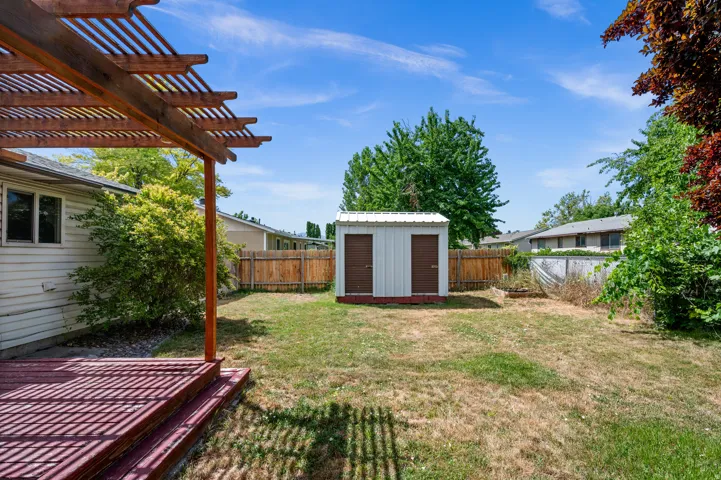 Expansive backyard featuring a wood-stained deck with a pergola, a storage shed with double brown doors, a wood privacy fence, and mature trees
