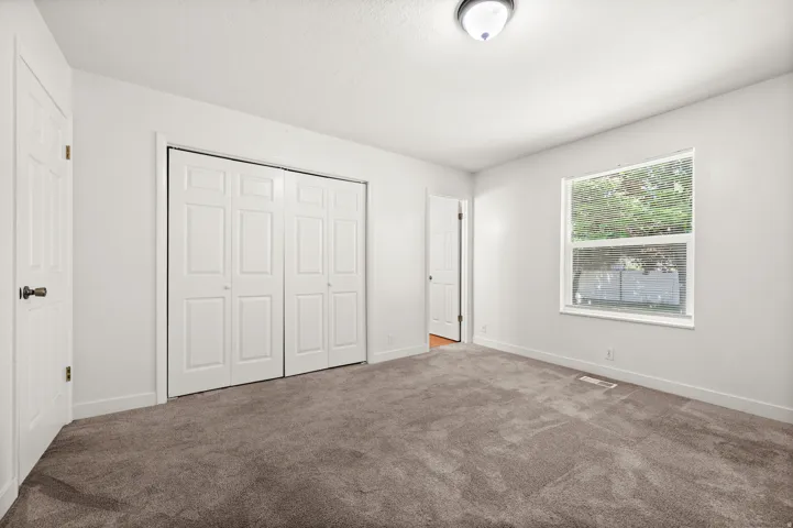 Bedroom featuring broadloom carpeting, crisp white walls, a multi-pane window, and bifold closet doors