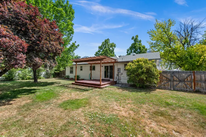 Spacious backyard featuring a wooden deck with a pergola, mature trees, and a privacy fence