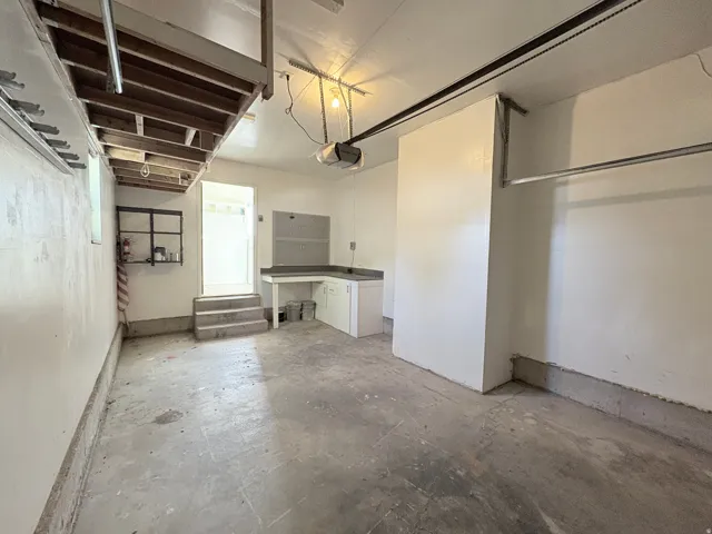 Spacious garage with concrete flooring, built-in shelving, a dedicated workbench with cabinetry, and an overhead storage area