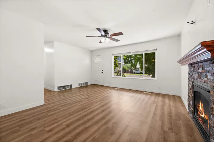 Living space featuring wood-finish flooring, a stacked stone fireplace with a wood mantle, a ceiling fan, and a large window