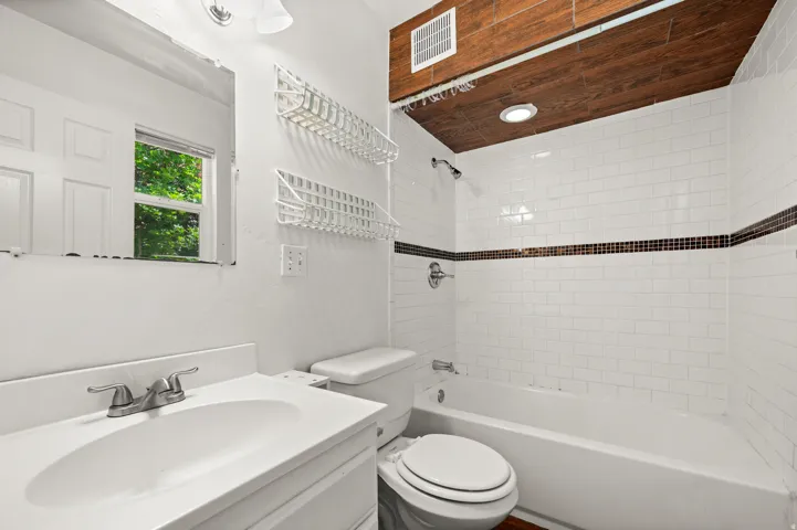 Bathroom featuring a white subway tile shower with a dark accent band, wood-finish ceiling, recessed lighting, and a white vanity with an integrated sink