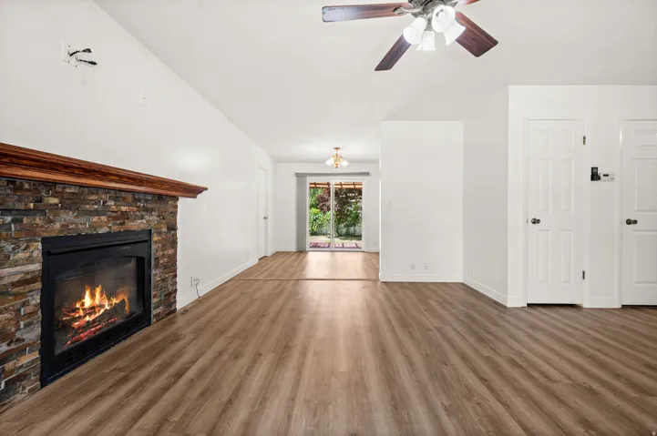 Spacious interior featuring wood-finish flooring, a stacked stone fireplace with wood mantle, and a vaulted ceiling with a ceiling fan