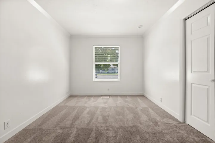 Bright room featuring a window with horizontal blinds, neutral wall paint, white trim, and patterned carpet flooring