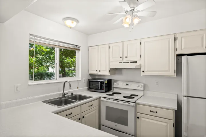Kitchen featuring white cabinetry with dark hardware, a double basin stainless steel sink with a gooseneck faucet, light-toned countertops, and a white electric range