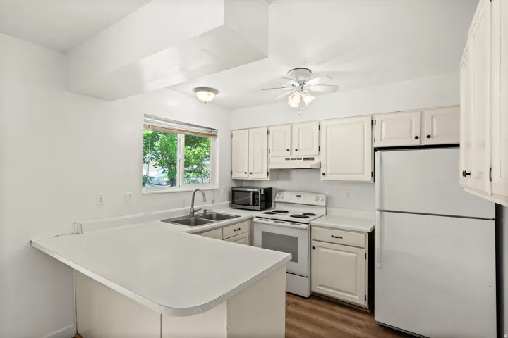 Efficient kitchen featuring white cabinetry, light-toned countertops, a double basin sink, and wood-finish flooring