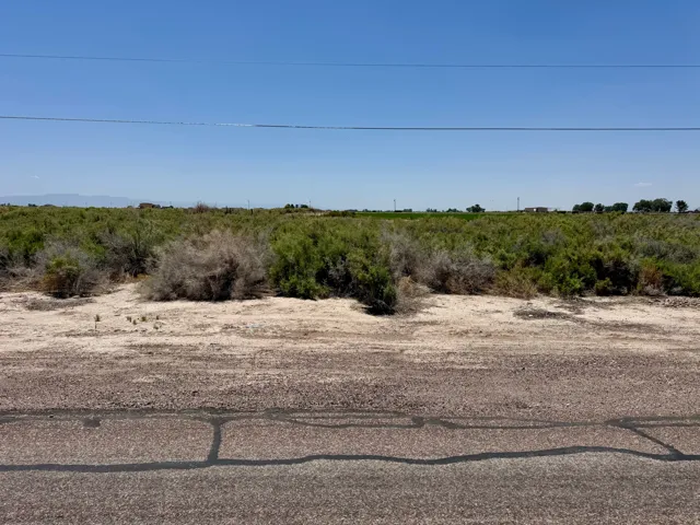 Expansive undeveloped land with natural vegetation and distant structures under a clear sky