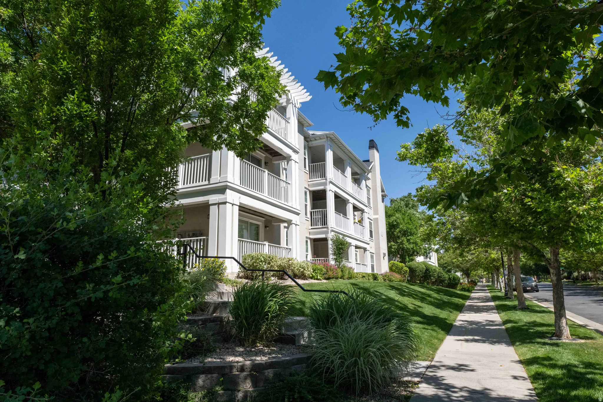 3rd story condo unit #111 to the left,  featuring 2 balconies with white railings, a pergola-style roof accent, and a light-colored facade